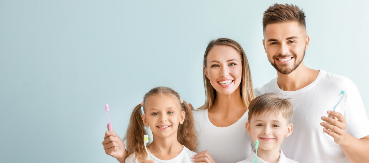 Smiling family of four holding toothbrushes after seeing family dentist in Norwood