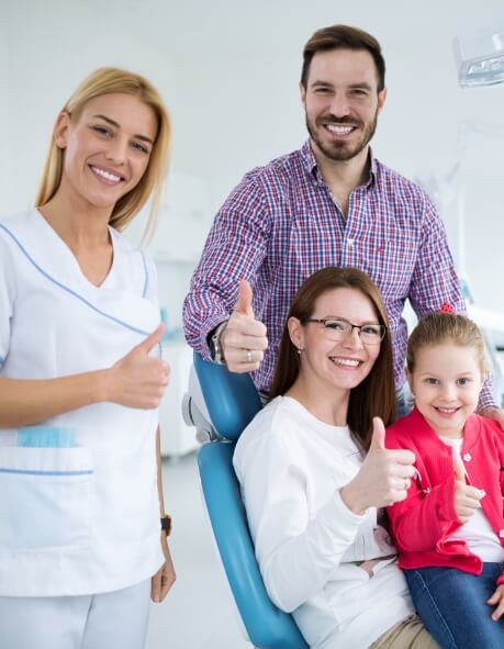 Family of three giving thumbs up with dental team member