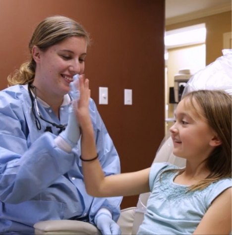 Young girl in dental chair giving high five to her dentist in Norwood