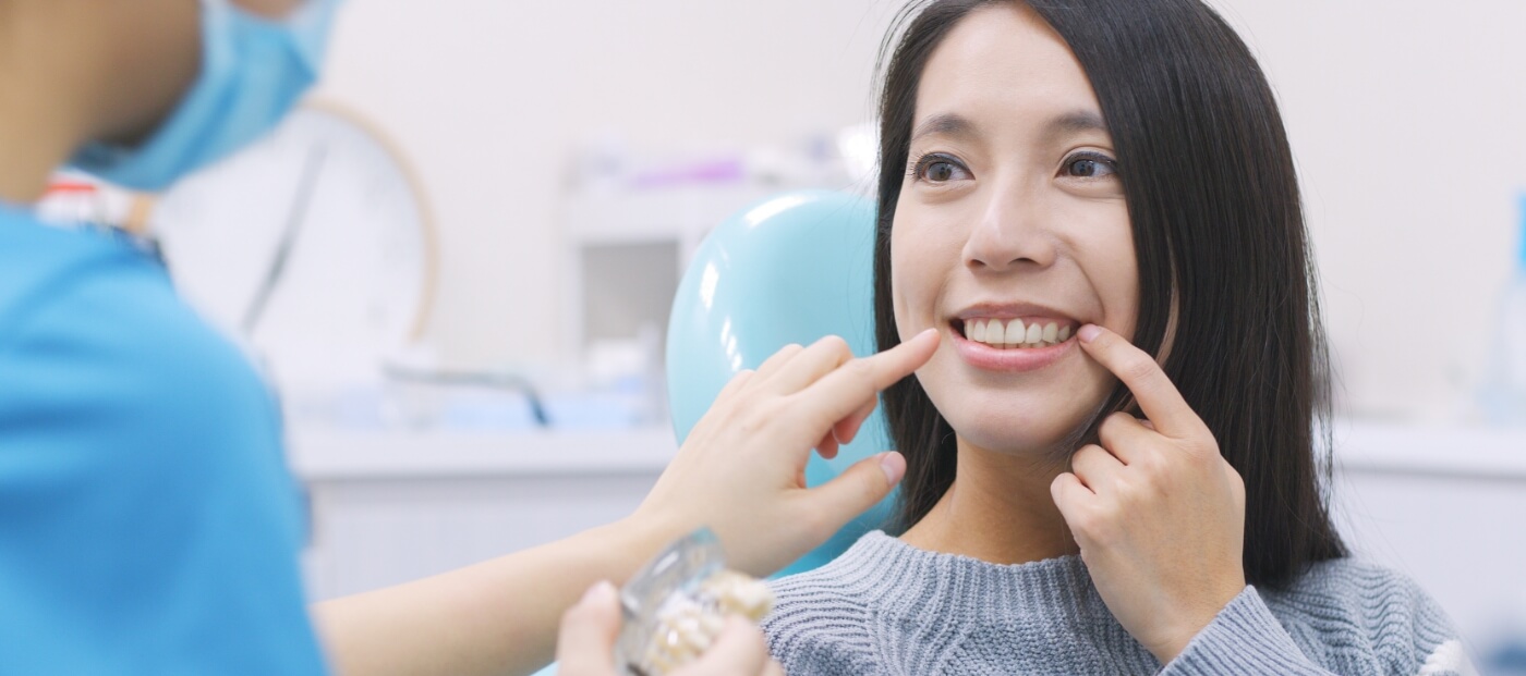 Dental patient pointing to her smile after replacing missing teeth in Norwood