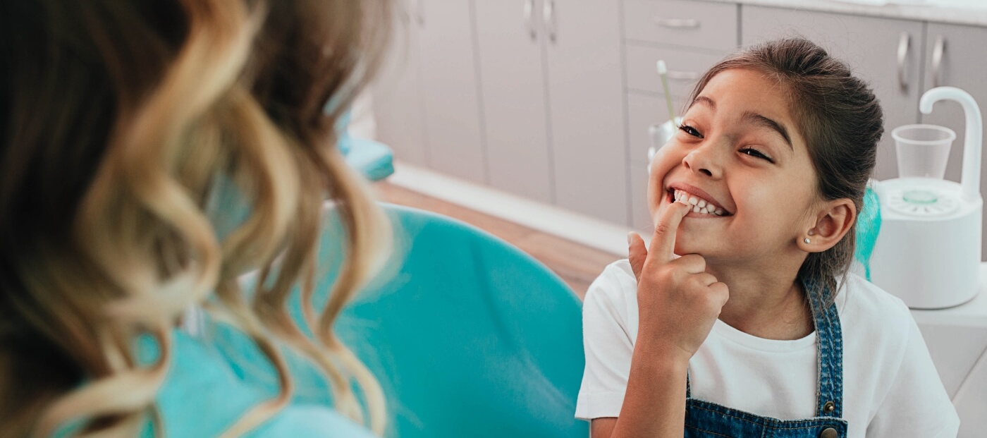 Young girl in dental chair pointing to her smile after restorative dentistry