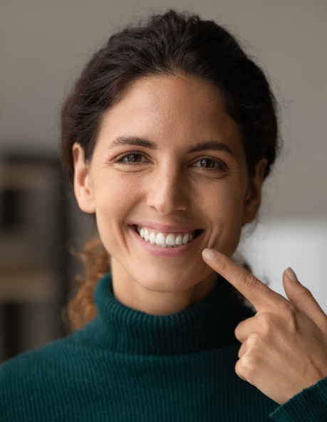 Woman in dark green sweater pointing to her smile