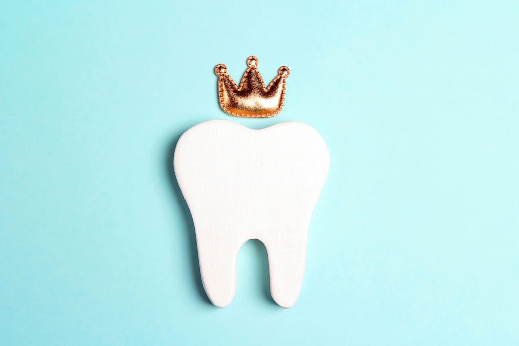 Large cutout tooth laying flat on teal surface with small golden crown